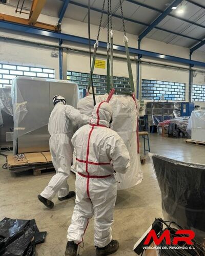 Operarios especializados en la retirada de amianto, equipados con trajes de protección, trabajando en una nave industrial.