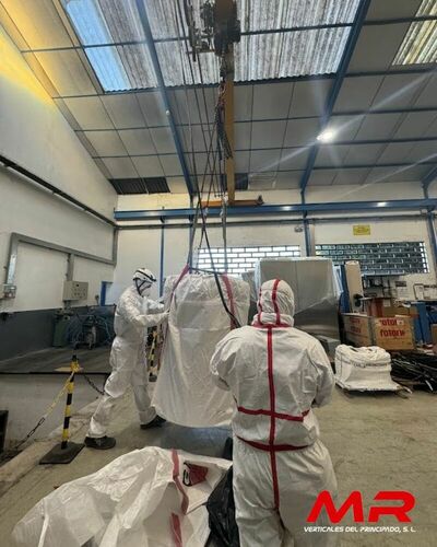 Operarios especializados en la retirada de amianto, equipados con trajes de protección, trabajando en una nave industrial.