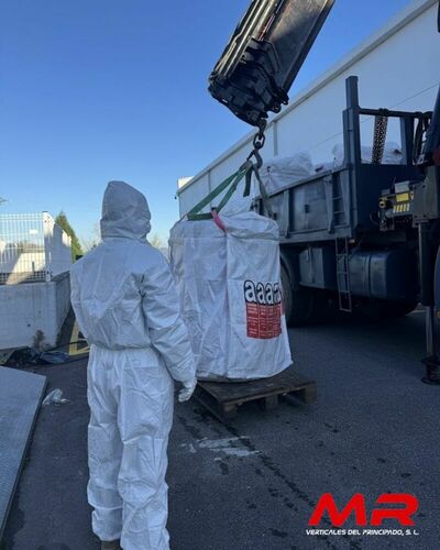 Operarios especializados en la retirada de amianto, equipados con trajes de protección, trabajando en una nave industrial.
