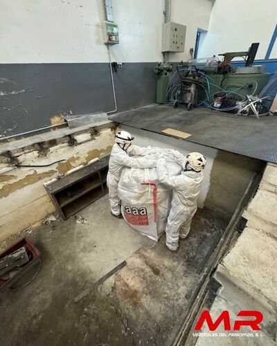 Operarios especializados en la retirada de amianto, equipados con trajes de protección, trabajando en una nave industrial.