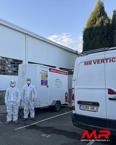 Operarios especializados en la retirada de amianto, equipados con trajes de protección, trabajando en una nave industrial.